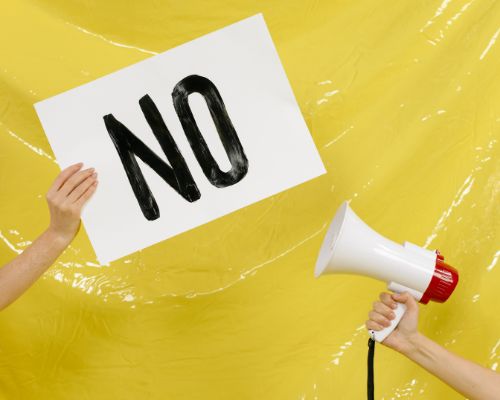 One person is holding a sign that says "no," another is holding a megaphone (Success for the Athletic-Minded Man podcast episode #451 The Art of Saying No: Setting Boundaries for Success and Sanity)